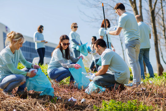 group of people doing community work and cleaning up a grassy area with tools and trash bags