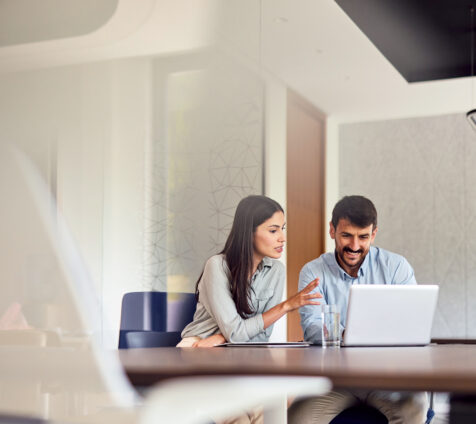 Two young professionals collaborating on a project, engaging with a laptop and exchanging ideas in a bright, modern office space filled with energy and creativity